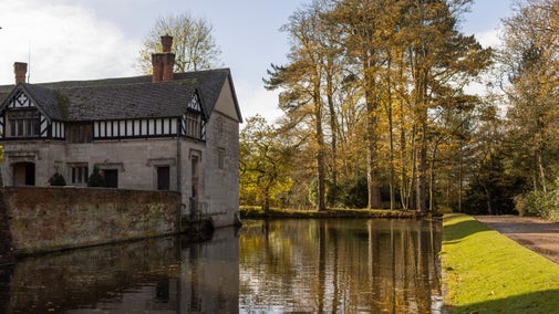 Autumn trees reflected in water with a building on the edge of the water to the left
